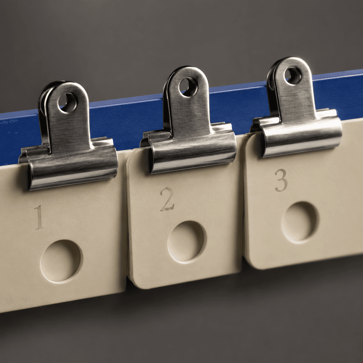 Macro photograph of brushed metal binder clips gripping cream numbered card tags